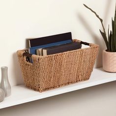 a wicker basket with books and magazines on a shelf next to a potted plant