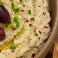 a bowl filled with hummus and olives on top of breadsticks next to crackers