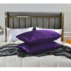 two purple pillows sitting on top of a bed next to a night stand and lamp