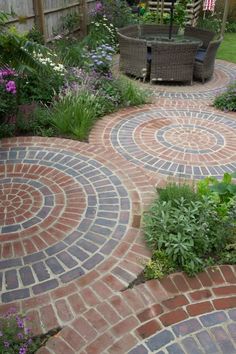 an outdoor patio with brick pavers and seating area in the center, surrounded by flowers and greenery