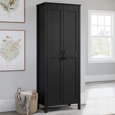 a black armoire sitting next to a window in a room with pictures on the wall