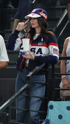 a woman holding a coffee cup while standing next to a man in a baseball cap