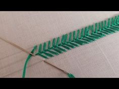 a close up of a piece of fabric with green thread on it and a needle in the middle