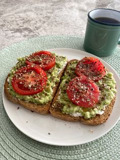 two slices of toast with avocado and tomatoes on it next to a cup of coffee