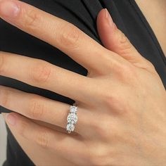 a woman's hand wearing a three stone diamond ring