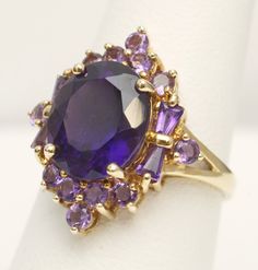 Signed Heng Ngai Amethyst Cluster Cocktail Ring 14K Yellow Gold US Size 7 Weight: 4.3 grams Center Amethyst measures approx. 12mm x 10mm Head of Ring measures approx.  21.6mm x 18.9mm This is a pre-owned item in Good Condition. It does show signs of use/wear but there is still lots of life left to this ring. Please note: Monitors/cellphone screens are not all calibrated the same, so colors of stones may appear different in person. CAT E 23-92101 Jewelry 2024, Ring Cat, Amethyst Cocktail Ring, Prom Outfit, Heart Necklace Diamond, Gold Sign, Amethyst Gem, Purple Band, Amethyst Cluster