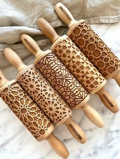 four wooden spoons with carved designs on them sitting on a marble surface next to a cloth