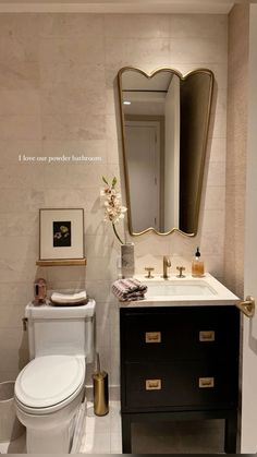 a white toilet sitting next to a sink in a bathroom under a large framed mirror