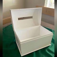 an empty white box sitting on top of a green cloth covered floor next to a window