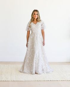 a woman in a white wedding dress standing on a rug with her hands behind her back