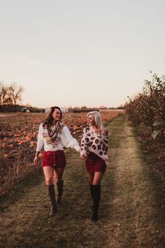 two women walking down a path in the middle of an apple orchard with their arms around each other