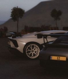 two cars parked next to each other in a parking lot with mountains in the background