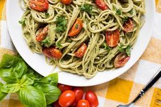 a plate of pasta with tomatoes and basil on the side next to a fork, knife and napkin