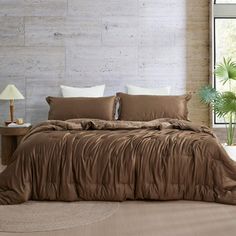 a bed with brown sheets and pillows in a room next to a large window that has a potted plant on it