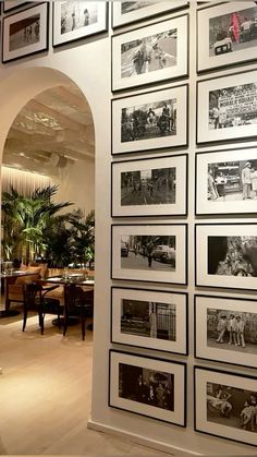 a wall full of black and white photos in a room with arches leading to the dining area