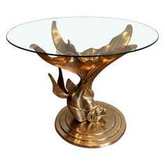 a glass table with gold colored metal birds on it's base and a circular glass top