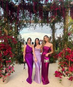 three beautiful women standing next to each other in front of some pink flowers and greenery