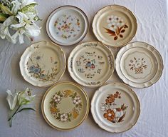 six plates with different designs on them sitting next to a flower vase and white flowers