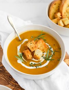 two bowls of soup with croutons and sour cream on the side next to bread