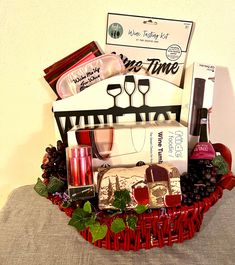 a red basket filled with wine, cheese and other items sitting on top of a table