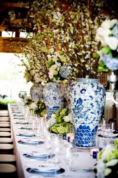 the table is set with blue and white vases, flowers, and plates on it