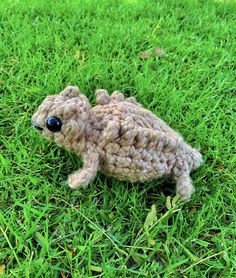 a small crocheted animal laying on top of grass in the middle of the day