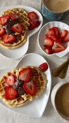 three heart shaped waffles topped with strawberries and chocolate sauce on white plates