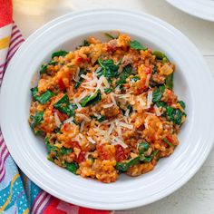 a white bowl filled with pasta and spinach on top of a colorful table cloth