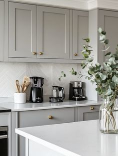 a kitchen with gray cabinets and white counter tops, coffee maker on the stove top