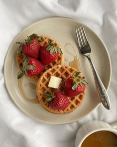 two waffles with strawberries and butter sit on a plate next to a cup of coffee