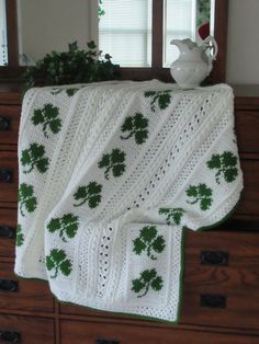 a white crocheted blanket sitting on top of a dresser next to a potted plant