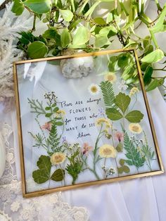 there are flowers and leaves in the frame on the table next to some white lace