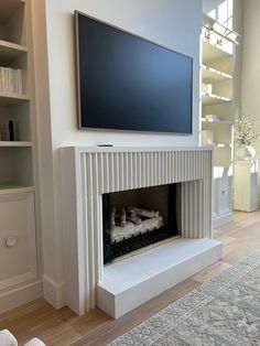 a flat screen tv mounted on the wall above a fireplace in a white living room