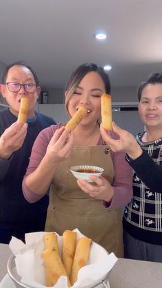 three people holding up hot dogs in front of them