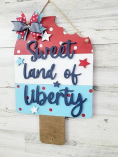 a sign that says sweet land of liberty hanging on a white wooden background with red, white and blue stars