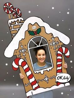 a woman holding up a cutout of a gingerbread house with candy canes