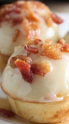 three small pastries on a white plate covered in bacon and icing, sitting next to each other