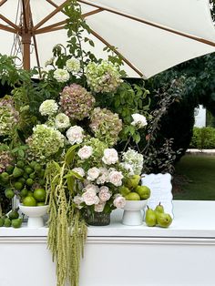 an arrangement of flowers and fruit is on display at a garden show in front of a white umbrella