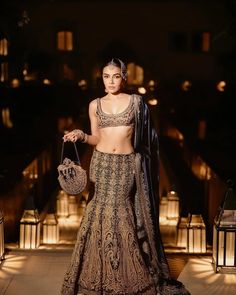 a woman in a brown and gold lehenga is posing for the camera at night