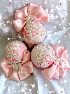 three pink ornaments with bows on them sitting on a white surface covered in snowflakes