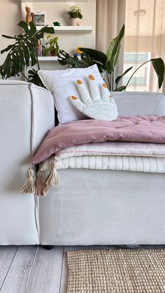 a white couch with pillows on it and some plants in the corner next to it