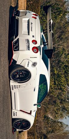 a white sports car is parked on the side of the road next to some trees