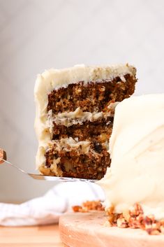 a piece of carrot cake with white frosting on a wooden cutting board next to a fork