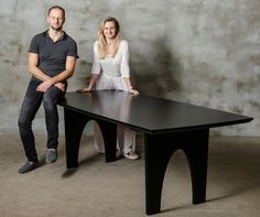 a man and woman sitting at a table posing for a photo in front of a concrete wall