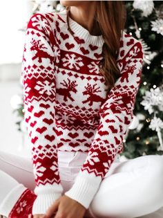 a woman sitting in front of a christmas tree wearing a red and white sweater