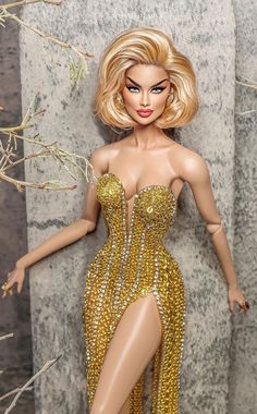 a barbie doll is posed next to a wall wearing a gold dress and high heels