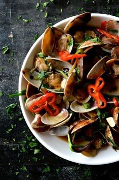 a white bowl filled with clams and peppers on top of a wooden table covered in parsley