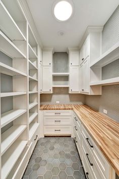 a large walk in closet with white cabinets and wood counter tops, along with hexagonal tile flooring