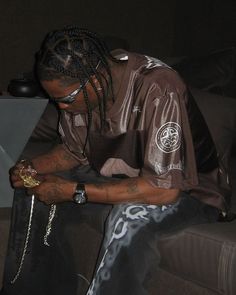 a man with dreadlocks sitting on a couch looking at his cell phone and holding a chain