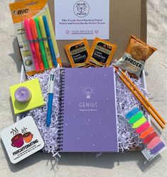 an open box containing pens, notebooks, markers and other items on the sand